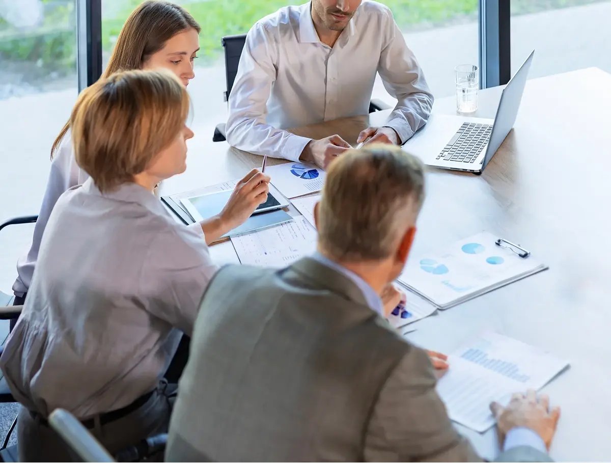 Team members discussing documents and data around a meeting table.