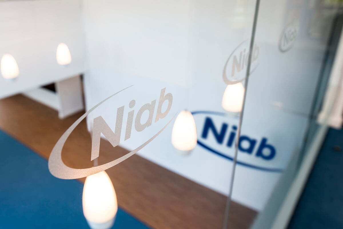 The NIAB logo etched into a frosted glass partition at NIAB's offices, lit by warm pendant lighting.
