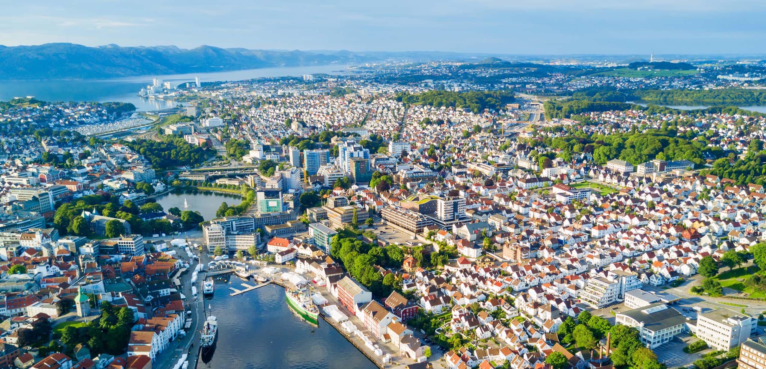 Aerial view of Stavanger, Norway, showing the city's white houses, central harbor, and fjord under a clear blue sky.