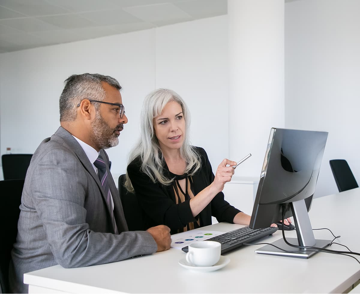 Two business colleagues reviewing charts and figures together on a desktop monitor during a working session.