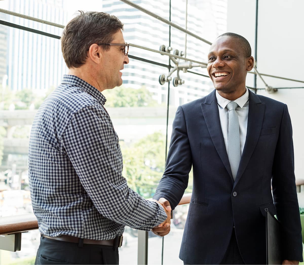 Two business professionals shaking hands in a modern office with a city skyline in the background.