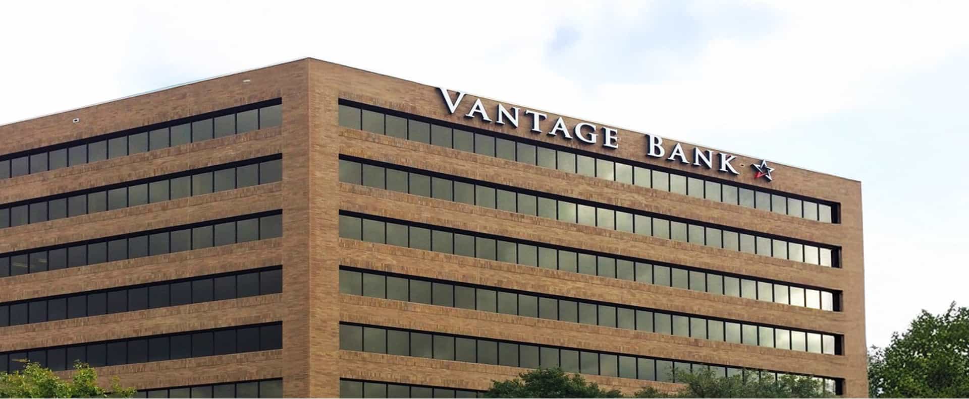 Close-up of the Vantage Bank headquarters tower corner, showing the raised metal 'Vantage Bank' lettering and red star logo mounted near the roofline.