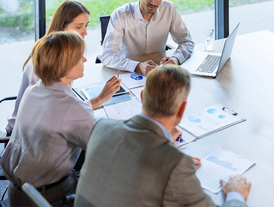 Business professionals collaborating around a meeting table with a laptop and printed charts